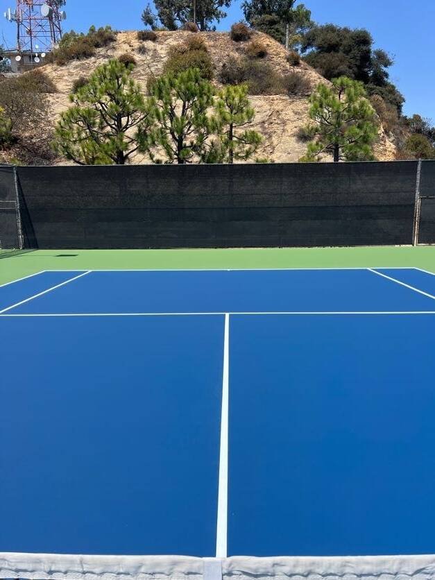 Outdoor blue tennis court with a hillside backdrop for private tennis coaching and match practice