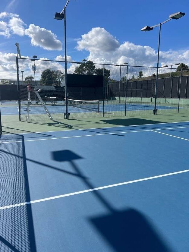 Blue outdoor tennis courts with nets, fencing and lights for tennis lessons and match-play practice