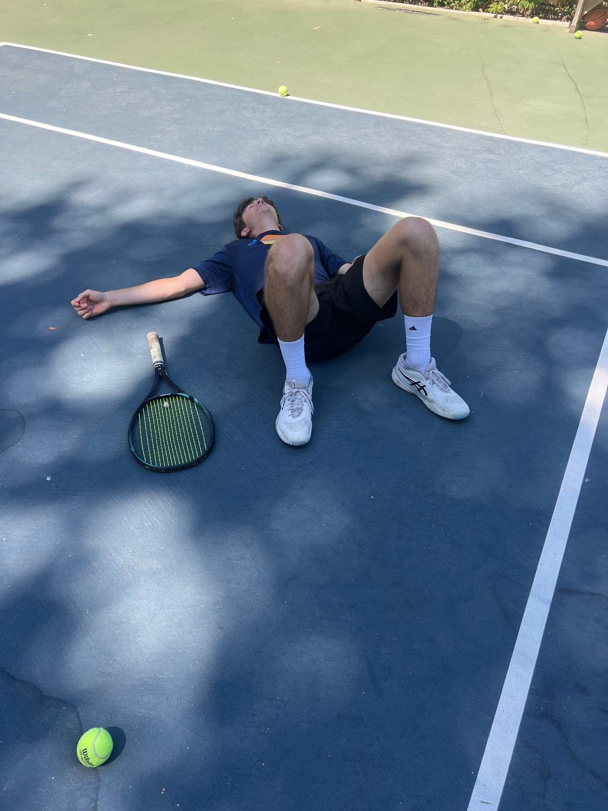 Tennis player resting on a Los Angeles court beside a racket during a beginner tennis practice session