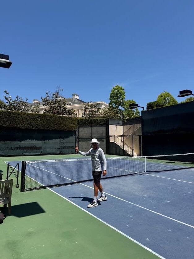 Tennis coach standing beside the net on a blue hard court for private and group tennis instruction in Los Angeles