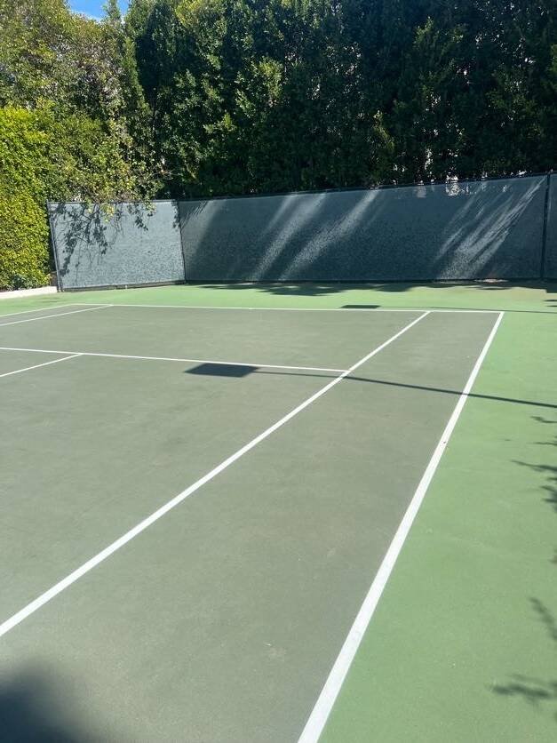 Green hard tennis court surrounded by trees for rally drills and tennis instruction serving Valley Village players