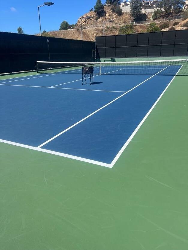 Tennis ball cart beside the net on a blue hard court prepared for rally and ball-control drills
