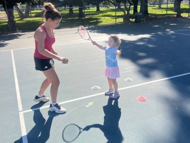 Coach helping a young beginner practice a tennis swing during a kids tennis lesson in Los Angeles